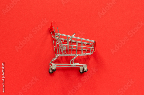 Small empty shopping trolley cart on red background. Concept sale. Top view Copy space