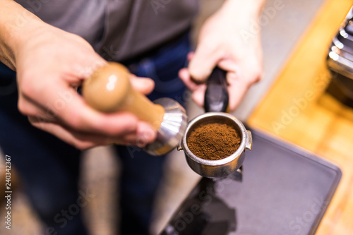 Barista with tamper and piston, portafilter in front of a grinder making espresso.