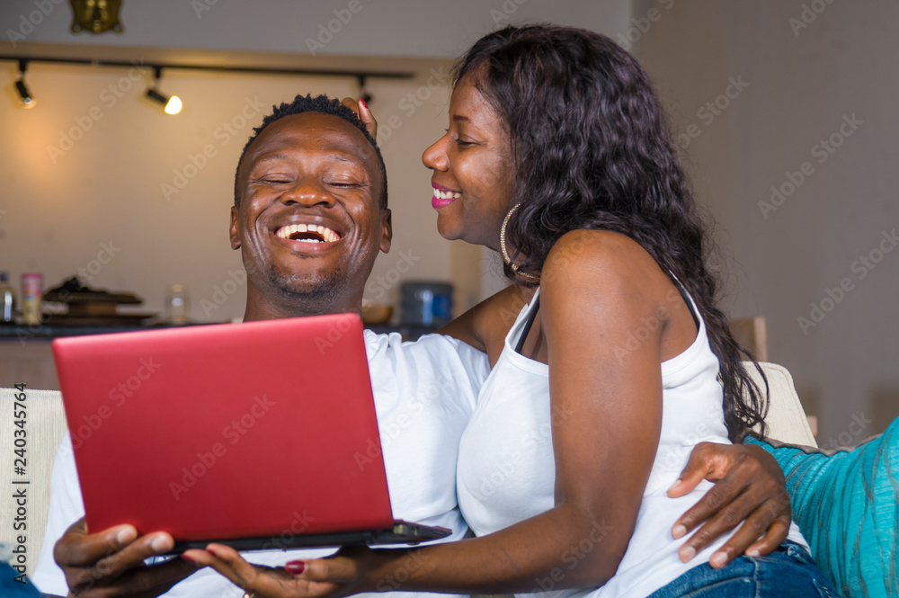 young happy and beautiful black afro American couple in love enjoying at living room sofa couch with laptop computer laughing and having fun networking