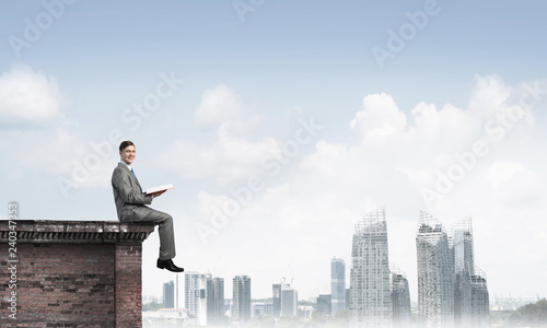 Wallpaper Mural Man on roof edge reading book and cityscape at background Torontodigital.ca