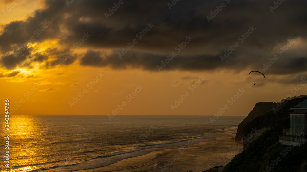 Obraz premium Lonely paraglide silhouette flying above the sea against golden sunset