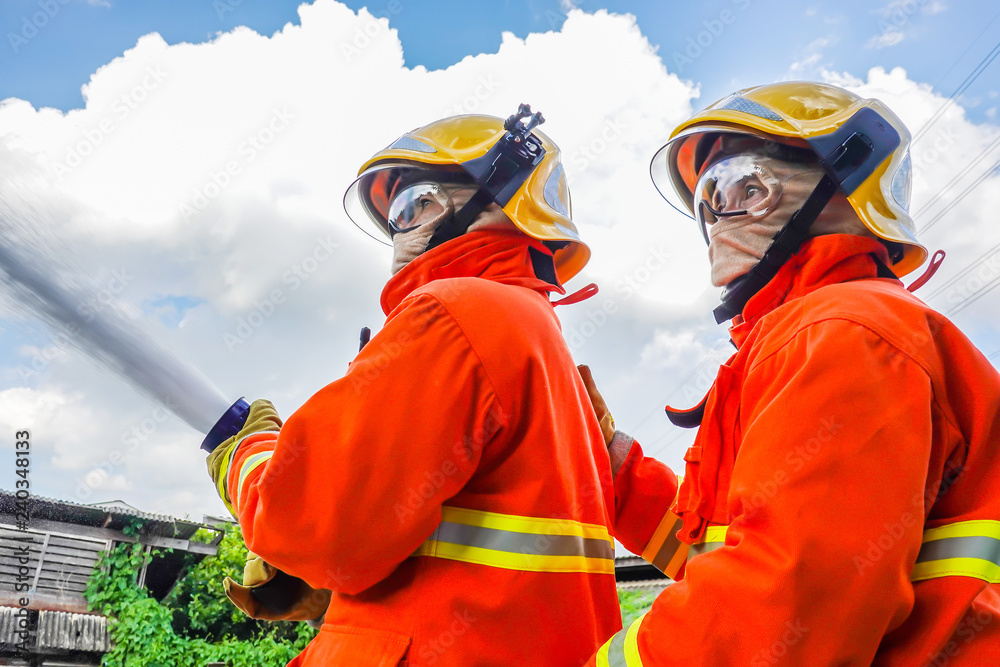 Fototapeta premium Two fireman trainning in fire fighting suit spraying water to fire surround on house background
