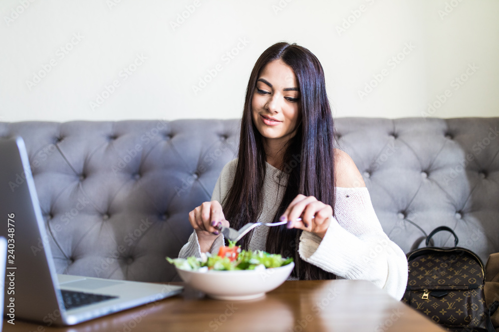 Young pretty woman enjoying salad sitting with laptop at cafe Young pretty woman enjoying salad sitting with laptop at cafe
