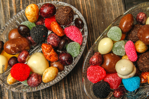 Fototapeta Naklejka Na Ścianę i Meble -  Different candies in a crystal bowl on old wooden table. Multi colored gummy candy coated with sugar, chocolate and fruit candy.