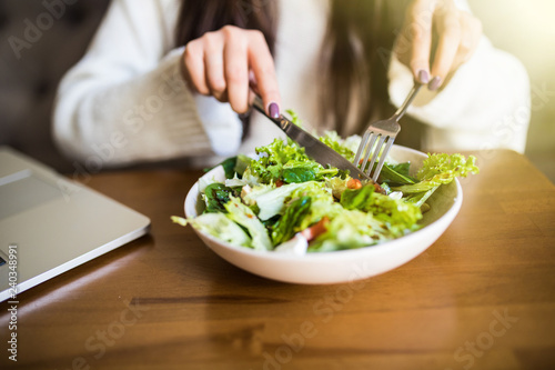 Close up attractive woman hand holding fork and spoon to eating vegetable salad at lunch in cafe. Healthy and vegetarian food.