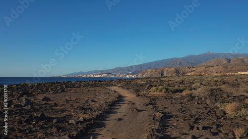 Path through the landscape of Malpais de la Rasca, a natural reserve close to Palm-Mar town, with views towards Atlantic Ocean and the tourist resort Los Cristianos, Tenerife, Canary Islands, Spain 