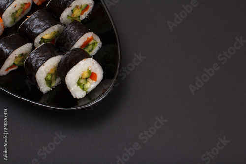 Sushi rolls in nori seaweed sheets on plate with black background.