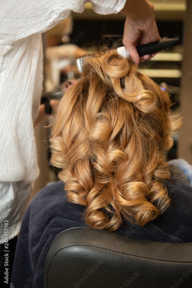 Hairdresser making styling with beautiful curls while girl sits in chair.  Fabulous volume blonde hair in beauty salon. Stock Photo | Adobe Stock