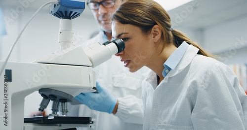 Portrait of female scientist analyzes a samples to extract the DNA and molecules with microscope in laboratory. Concept: research,biochemistry, pharmaceutical medicine