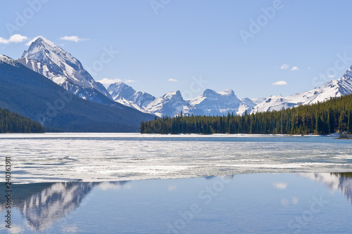 Snow covered Rocky mountains peaks reflected on the half frozen Maligne lake - Jasper national park, Alberta, Canada. The shot was taken in late spring.