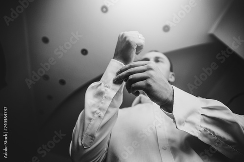 Stylish groom putting on white shirt, getting ready in the morning near window in soft light, before wedding ceremony. Bottom top view © sonyachny