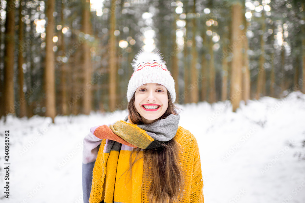 Obraz premium Portrait of a young woman dressed in bright winter clothes standing in pine forest during the winter time