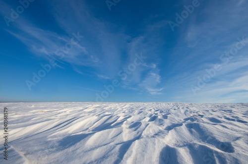 White snow and blue sky with clouds as background. Patterns in the snow, created by the wind.