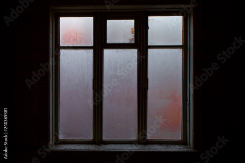 a lighted window in the black room of an abandoned house  a clear outline  glass covered with frost 
