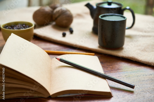 Close-up of notebook with blank papers and green pencil on it with coffee drink in the background