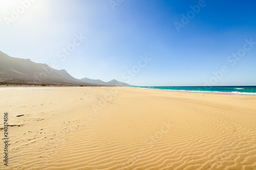 Fuerteventura, Canary Islands, Spain. Cofete beach with endless horizon and traces on sand. Volcanic hills in the background and Atlantic Ocean.