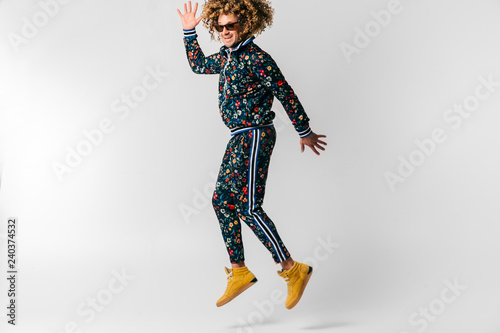 Adult positive smiling funky man with curly hair style in suglasses and vintage clothes posing on white studio background. Funny portrait of stylish male person. 80s fashion. Unusual eccentric guy. © benevolente