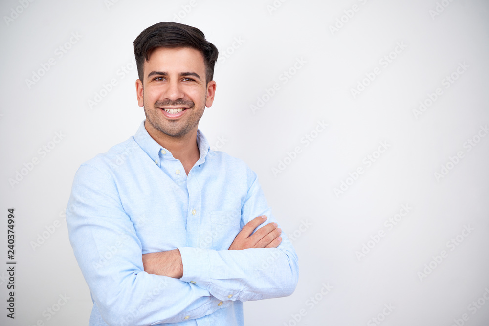 Portrait of happy dark haired man wearing blue shirt standing with arms crossed on white background Portrait of happy dark haired man wearing blue shirt standing with arms crossed on white background