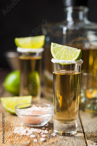 Mexican Gold Tequila shots with lime and salt on wooden table over black background