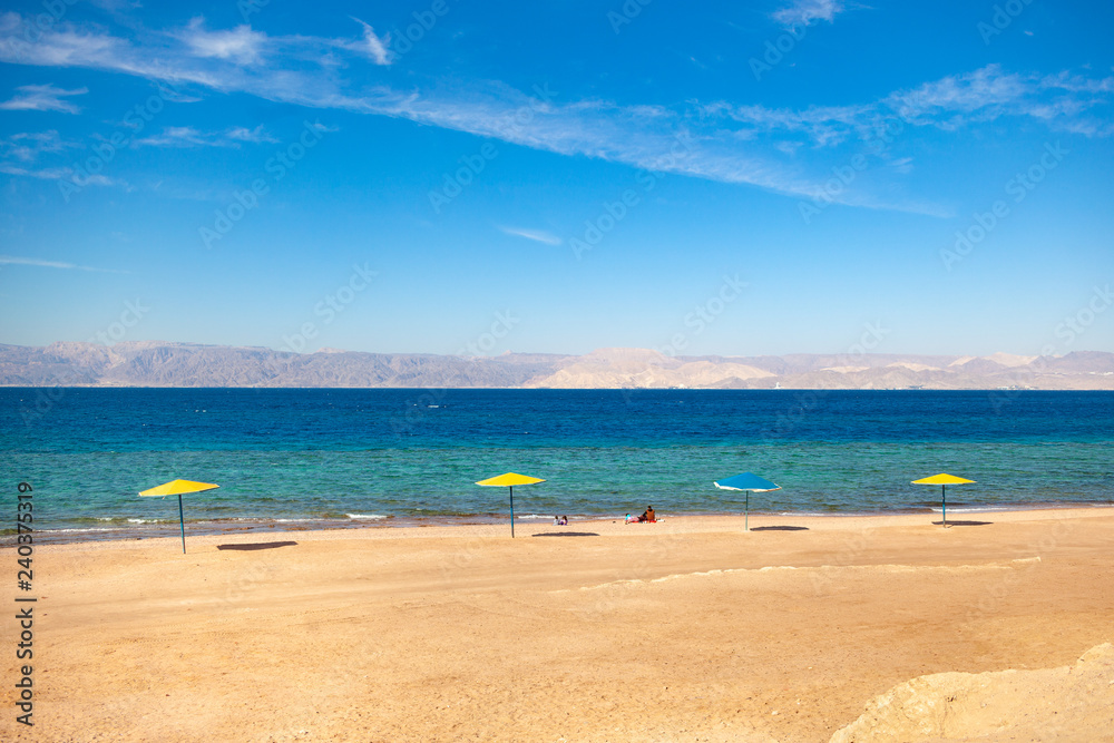 Obraz premium Beach on the shore of the Red Sea. Umbrellas, water and beach. Resort in the Aqaba, Jordan next to Israel Ejlat.