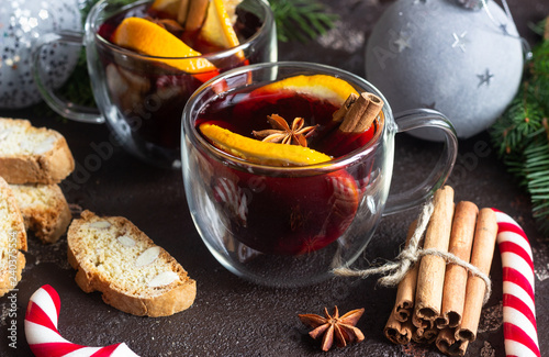 Glass cups of hot mulled wine or gluhwein with spices and orange pieces on dark brown background. Christmas mulled wine. Traditional drink on winter holiday. Copy space.