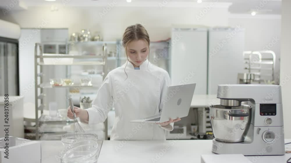 Young head cook in professional uniform is using her laptop Young head cook in professional uniform is using her laptop