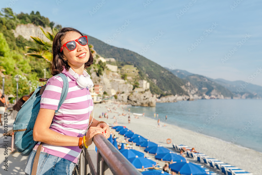 Happy young woman with backpack enjoying beautiful seascape in Italy. Vacation and travel in Cinqueterre national park, mediterranean sea.