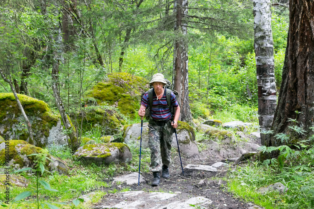 Obraz premium A tourist goes along a wide path. Male traveler climbs uphill on a walking path.