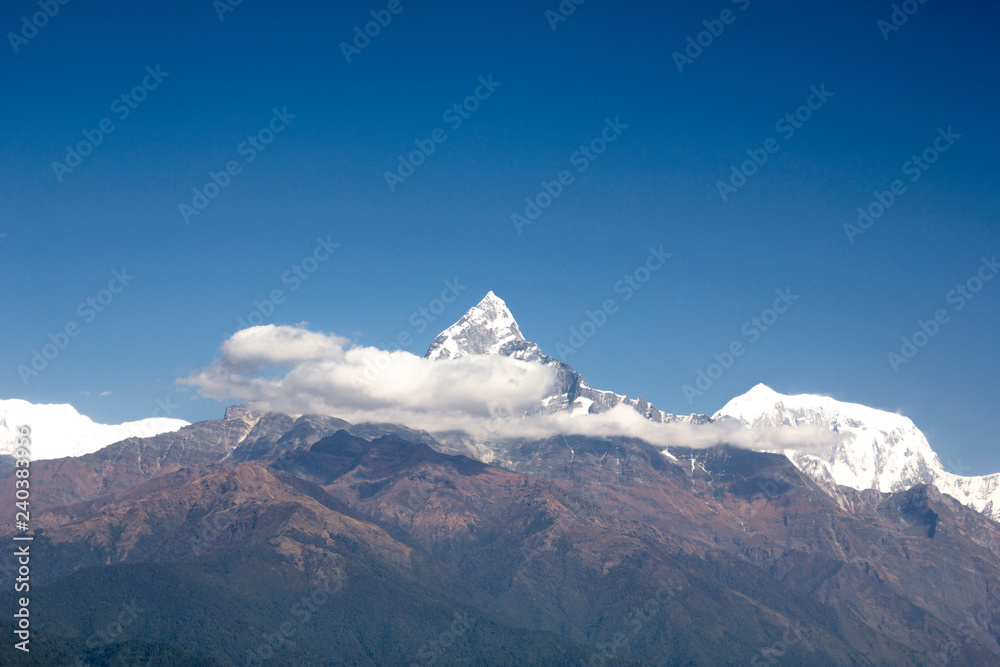 the green slope of Mount Annapurna with a snowy peak Machapuchare and white clouds against a clean blue sky. Nepal Himalayas.