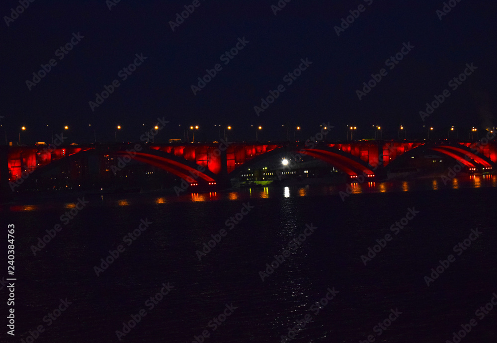 Night bridge over the Yenisei river. Reflection of lights in water. The sights of the city of Krasnoyarsk.