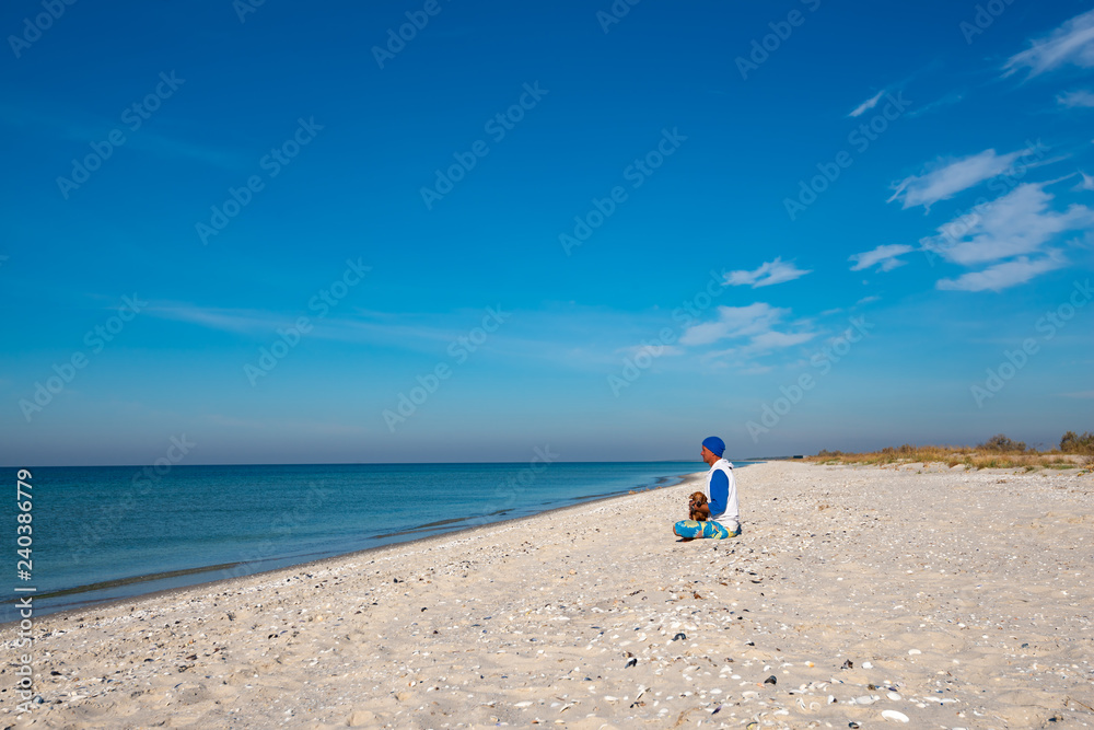 Traveler with funny dog sits on the deserted beach