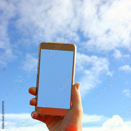 iphone in hand against the blue sky summer sunny day, space for text