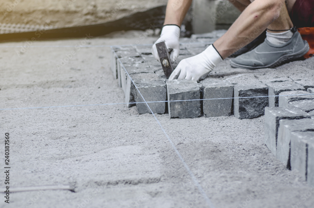 Worker lays gray granite pavement tiles on the marked site. Arrangement of urban environment. Repair of city roads Worker lays gray granite pavement tiles on the marked site. Arrangement of urban environment. Repair of city roads