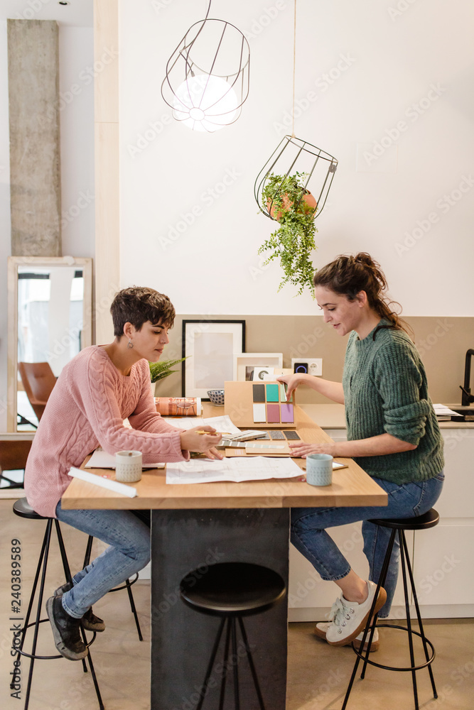 Side view of two women interior designers discussing about blueprints Side view of two women interior designers discussing about blueprints