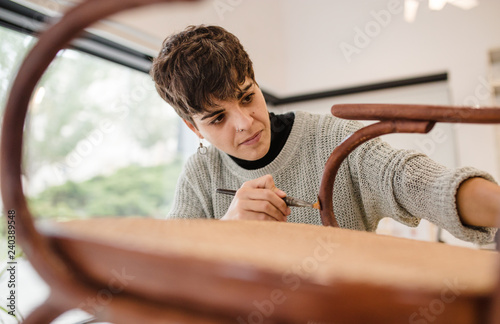 Front view of young furniture restorer varnishing an old wooden chair photo