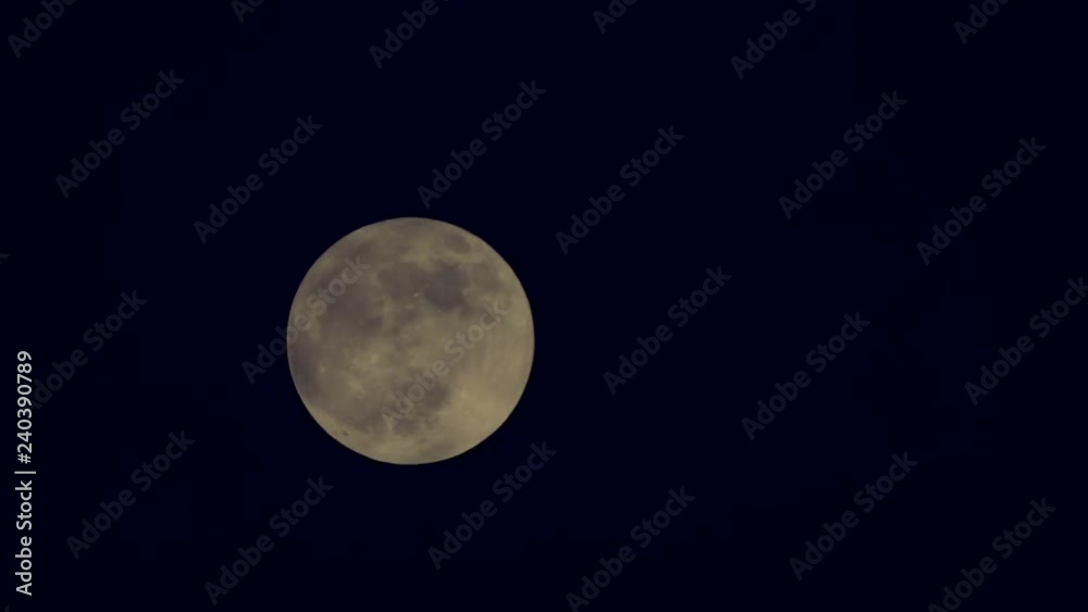 The moon pavilioned and coming out from behind dark clouds at black night sky. Full moon slowly swims in sky, cloud blotting out natural satellite at windy evening. Moon obscured by clouds in darkness