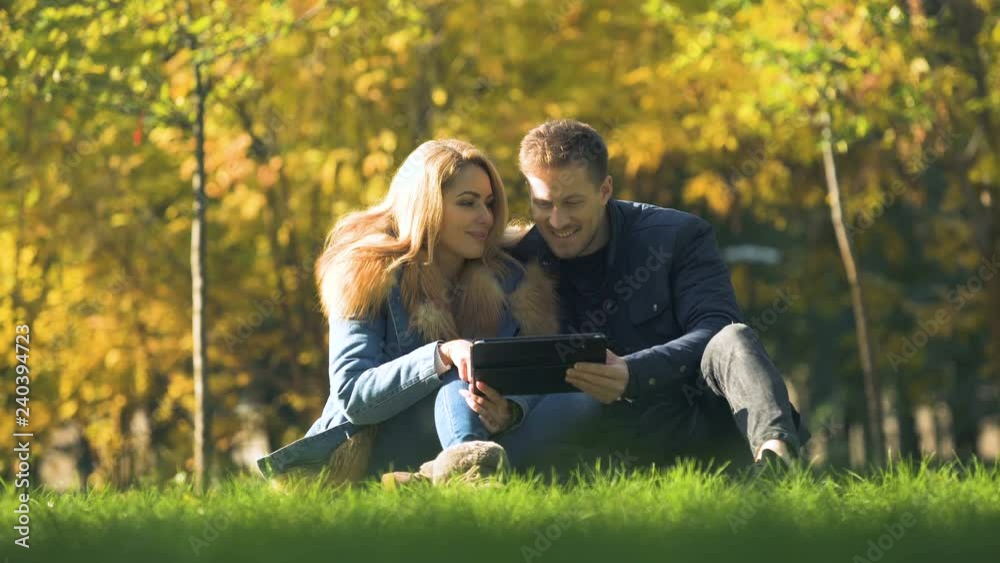 Couple shopping online, using tablet at autumn park, buying warm clothes in net Couple shopping online, using tablet at autumn park, buying warm clothes in net