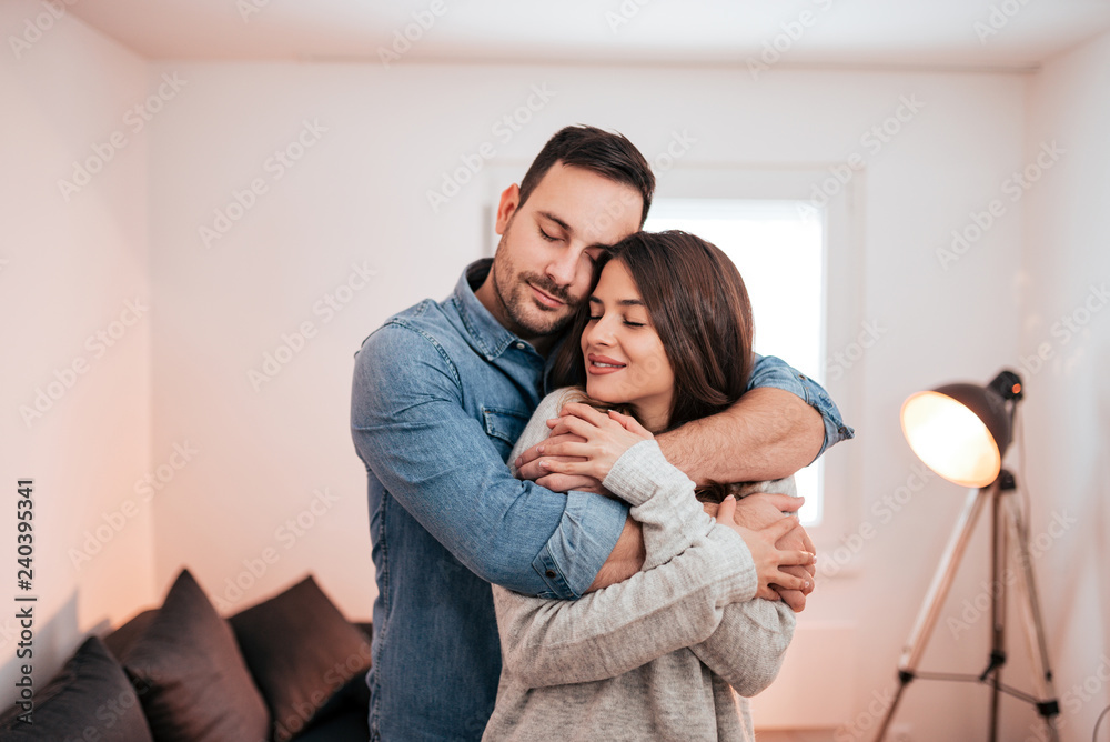 Young man embracing woman from back with eyes closed at home. Relationship goals. Young man embracing woman from back with eyes closed at home. Relationship goals.