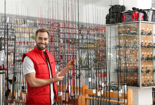 Salesman with fishing rods in sports shop. Space for text photo