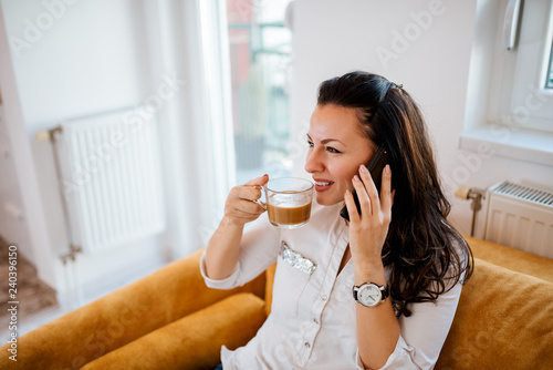 Young woman relaxing at home. Drinking coffee and talking on mobile phone.
