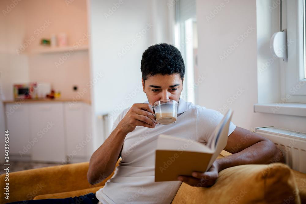 African american man drinking coffee and reading a book at home. African american man drinking coffee and reading a book at home.