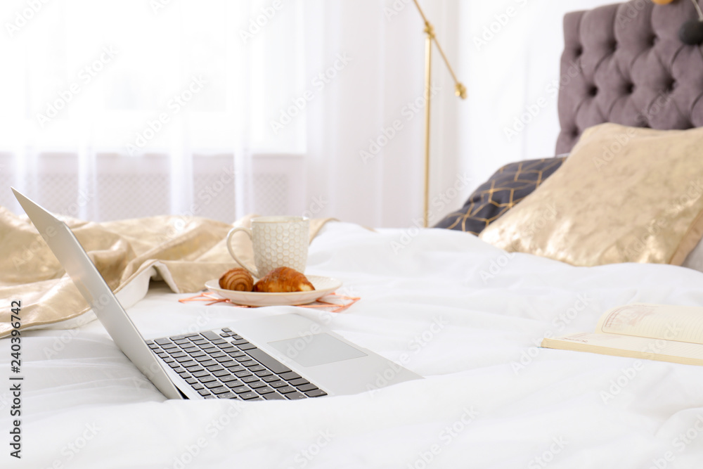 Laptop and breakfast on bed in stylish room interior