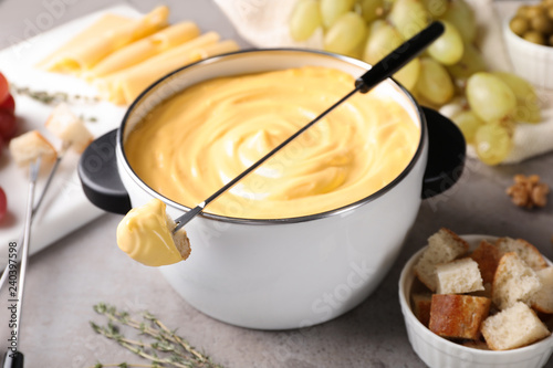 Pot of delicious cheese fondue and fork with bread on gray table