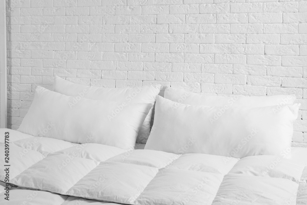 Large comfortable bed with pillows and blanket near white brick wall indoors. Stylish interior Large comfortable bed with pillows and blanket near white brick wall indoors. Stylish interior