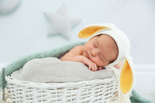 Adorable newborn child wearing bunny ears hat in baby nest indoors