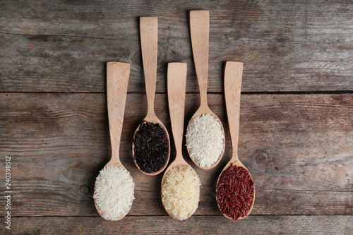 Flat lay composition with brown and other types of rice in spoons on wooden background