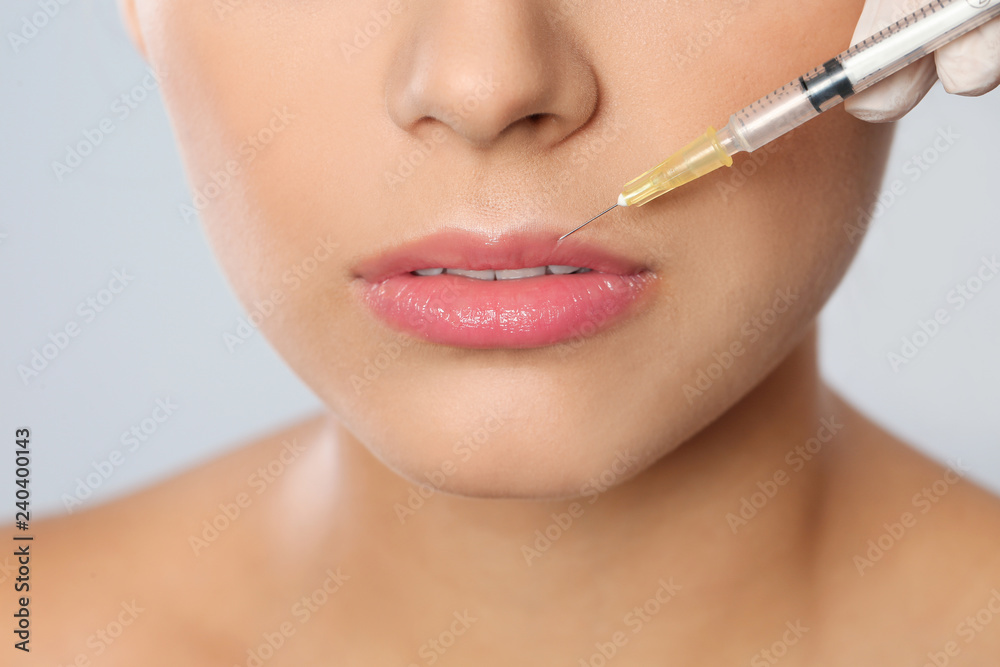 Young woman getting lips injection on grey background, closeup. Cosmetic surgery