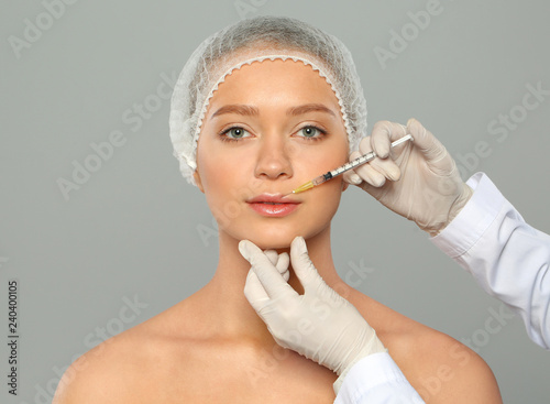 Young woman getting lips injection on grey background. Cosmetic surgery