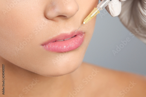 Young woman getting lips injection on grey background, closeup. Cosmetic surgery © New Africa