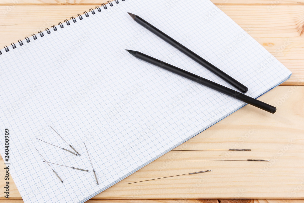 Silver needles for traditional Chinese medicine acupuncture lie on a note book, on a wooden table. Silver needles for traditional Chinese medicine acupuncture lie on a note book, on a wooden table.